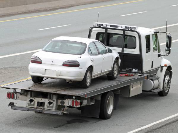 White flatbed truck providing a car removal service on the highway