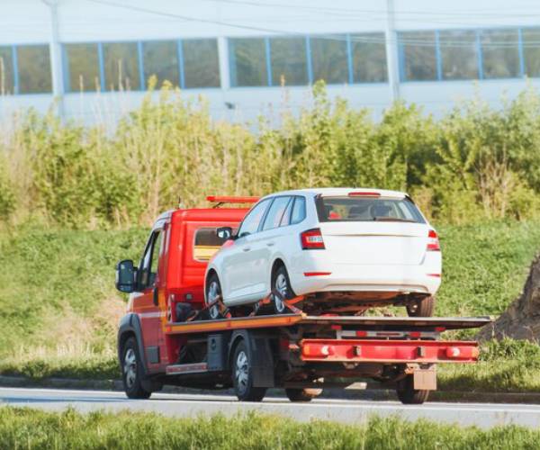 Truck towing services carrying white car on flatbed tow truck road